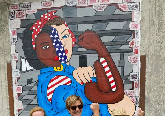 Three guests posing in front of Rosie the Riveter mural, doing her pose.