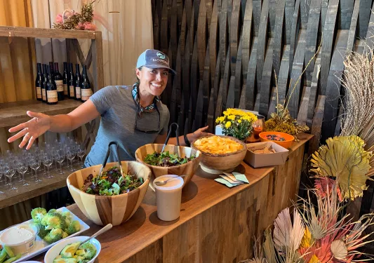 Leader behind lunch spread, gesturing to it.