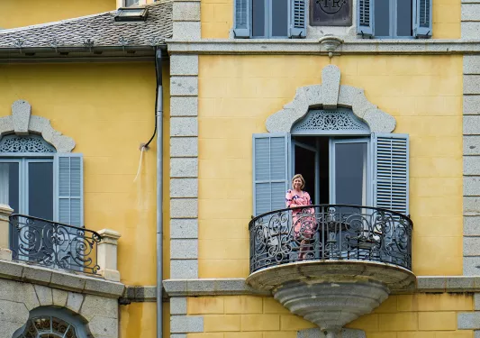Woman standing on balcony of yellow building. 