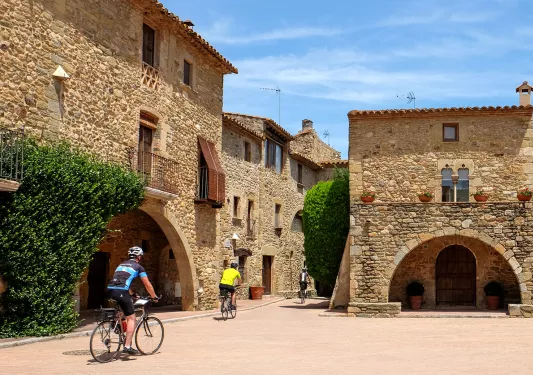 Two guests cycling through village, tan stone buildings all around.