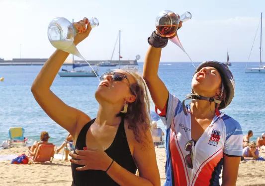 Two guests on beach, drinking from ornate wine glasses.