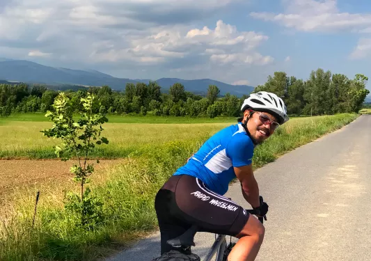 Guest cycling down grassy road, looking back at camera, meadow to left.