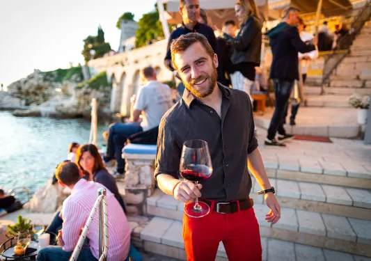 Man among group of other people, wine glass in hand, sunset.