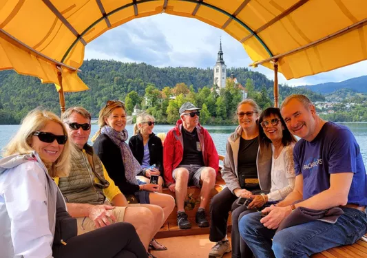 Group of guests on boat, forest, spire in distance.