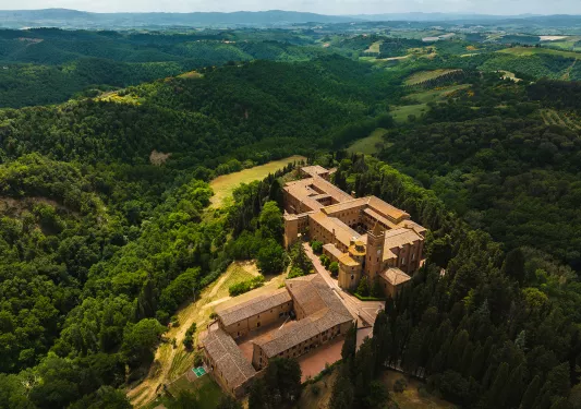 Bird's eye shot of Italian countryside, forests, castle, hills visible.