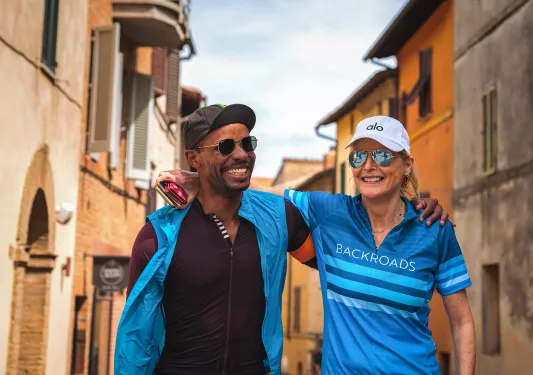 Two guests walking down Italian alleyway, arms over each other's shoulders.