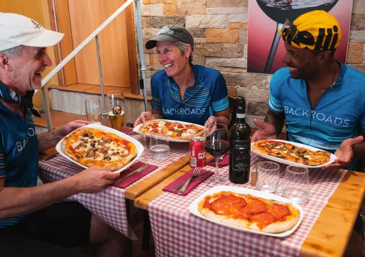 Three guests at lunch, pizzas in hand.