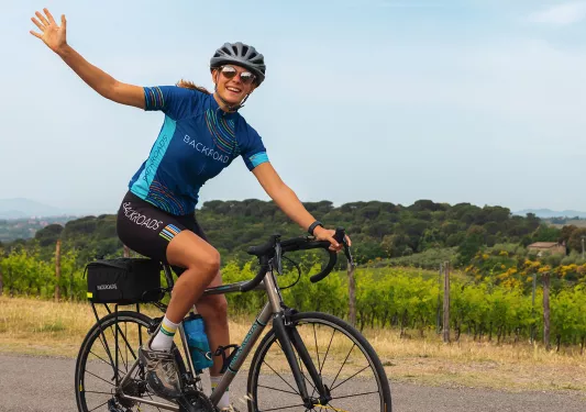 Guest cycling in countryside, waving to camera.