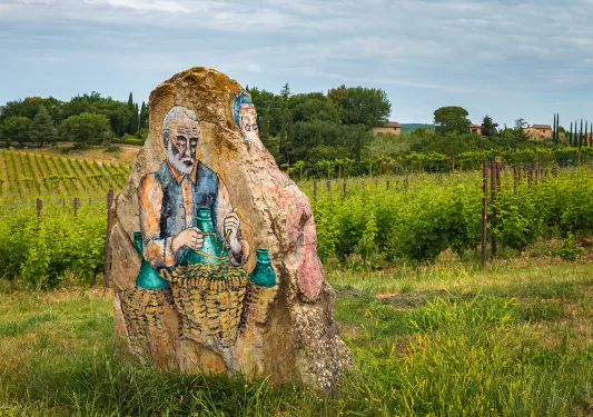 Shot of painting on craggy boulder, vineyard, villa in distance.