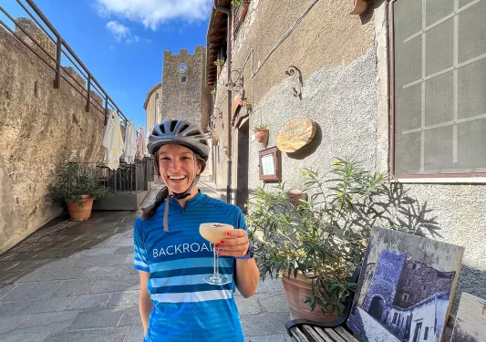 Guest in bike clothes holding cocktail, tan-stone walls surround them.