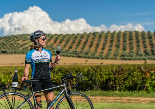 Backroads guest holding a glass of wine with a vineyard in the background.