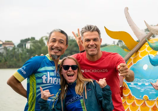 Three Backroads guests smiling and posing in front of a dragon boat in Vietnam