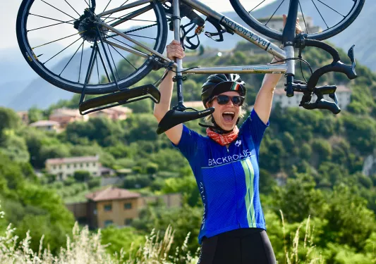 Guest in bike gear, holding bike above her head.