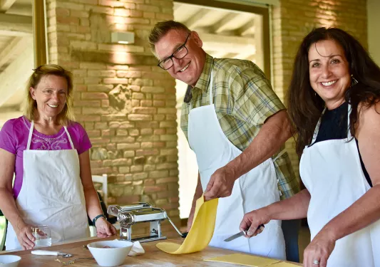 People smiling at the camera while rolling out pasta dough