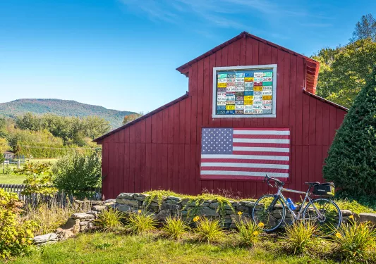 Shot of bike in front of red barn, US flag on barn wall.