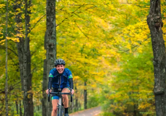 Guest cycling down fall road, facing camera and smiling.