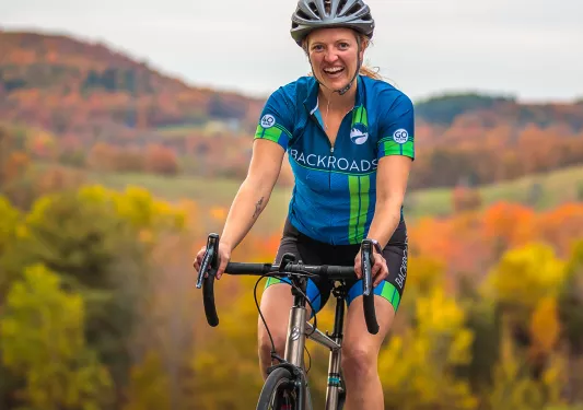 Guest cycling, smiling at camera, trees behind her.
