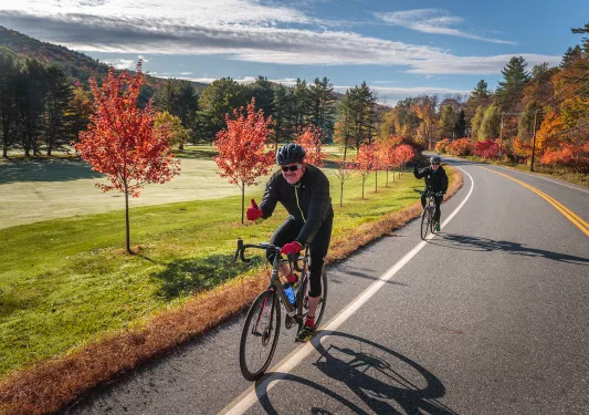 Two guests cycling down autumnal road, both giving thumbs-ups.