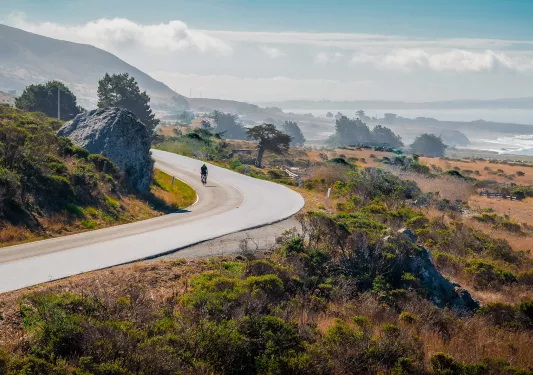 Coastal California vista, ocean and cliffs in background, cyclist in foreground.