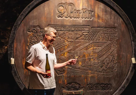 Man holding a bottle of wine in one hand and a glass with wine in the other in front of a very large wine barrel