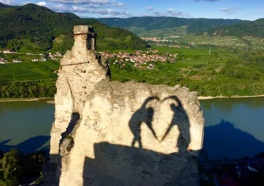 Shadows of two people making a heart with their arms.