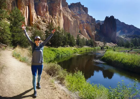 Guest with their arms over their heads, hiking next to a small river.