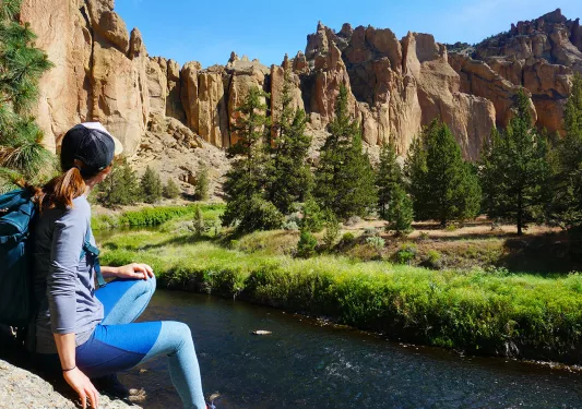 Guest sitting in front of small river, craggy rocks in background.
