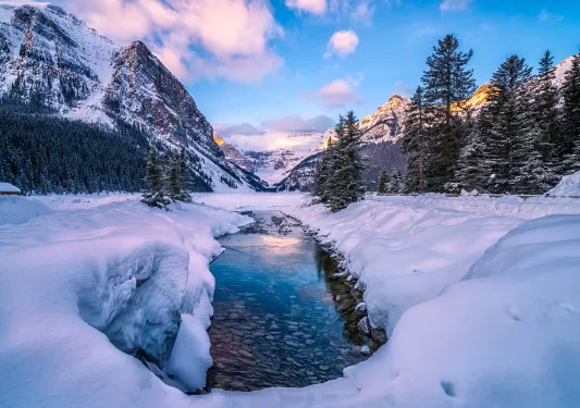 Wide shot of snowy valley, mountains, trees around.