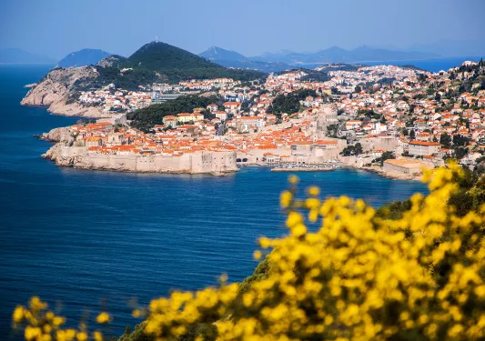 Wide shot of Dubrovnik coastline, blue ocean, white and tan houses.