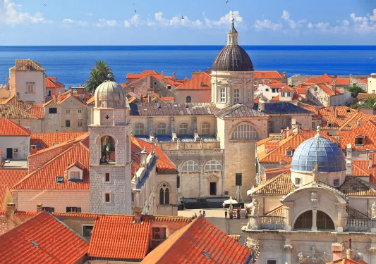 Wide shot of Dubrovnik coastline, blue ocean, white and tan houses.