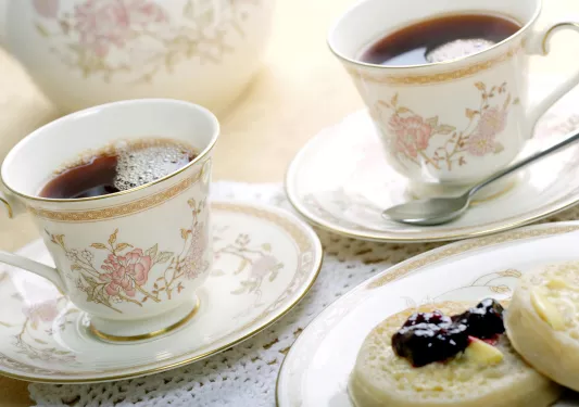 Ornate English cups of tea and english muffins with butter and jam.