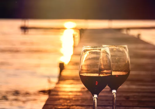 Two wine glasses sitting on pier, sunset in background.