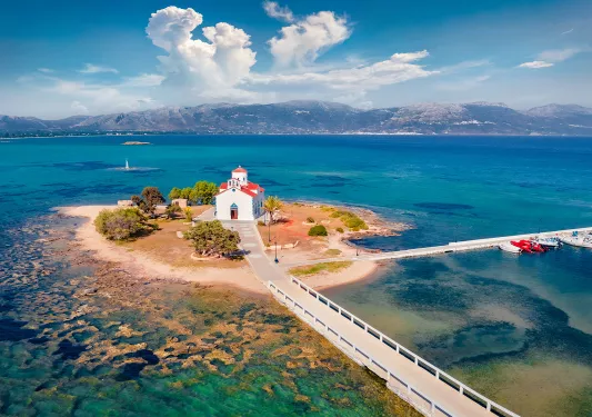 Shot of small island with church, two roads leading onto it, amidst ocean vista.