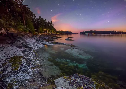 Wide shot of lake at sunset, large stars twinkling in the night sky.
