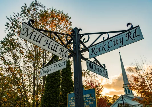 Rustic four-way street sign, sunset in background.