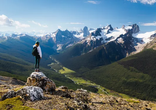 Guest standing on rocky hilltop, looking towards larger mountains.