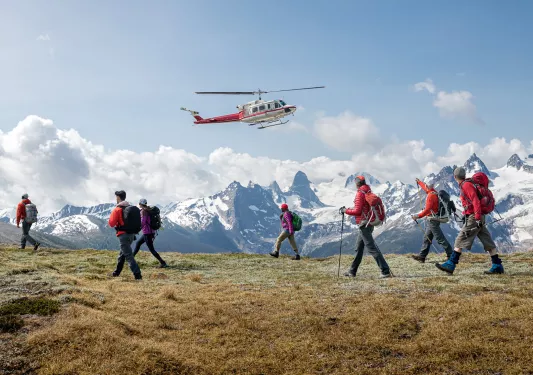 Group of guests beginning mountain hike , waving goodbye to helicopter.