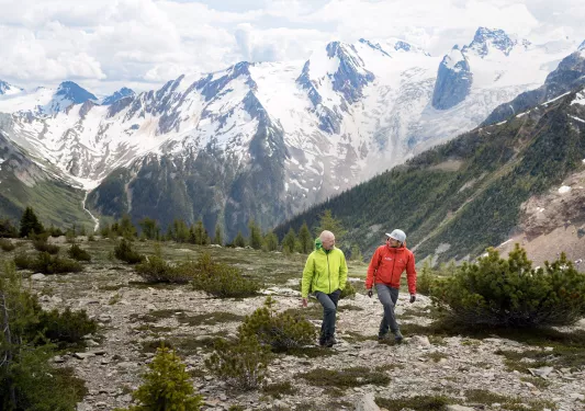 Two guests walking on hillside, Bugaboos in background.