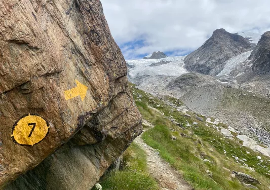 Painted trail marker on side of cliff, hiking trail in distance.