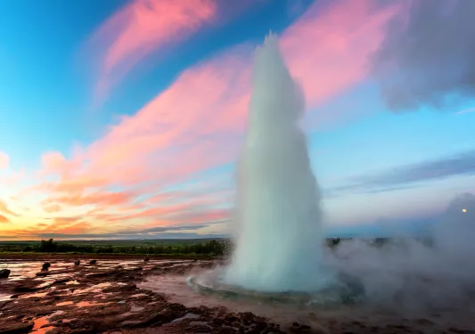 Shot of thermal geyser erupting, vibrant pink/blue sunset.
