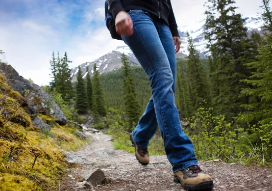 Ground shot of guest walking down muddy trail, forest, mountain behind them.
