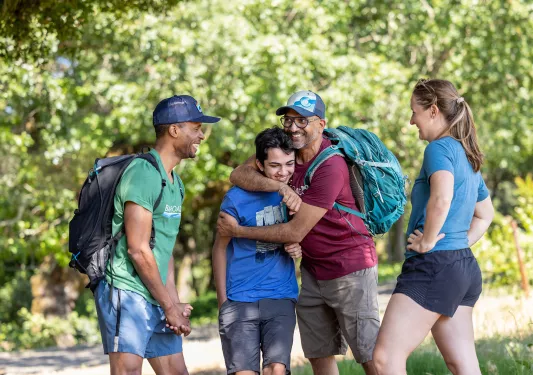 Four guests on the trail, smiling at each other, one is hugging another.