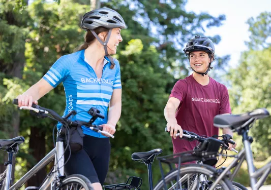 Two guests walking with their bikes, talking, both smiling.