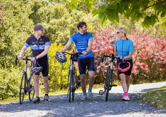 Three guests with bikes walking down gravel road, all talking.