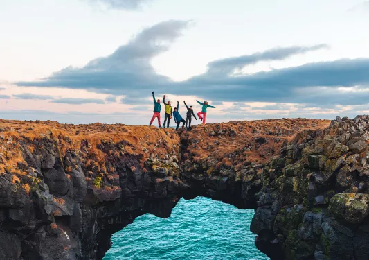 Guests posing on rock archway above ocean