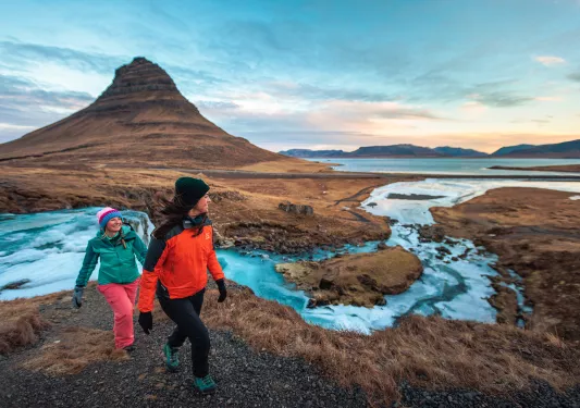 Two hikers walking along side stream of water in Iceland.
