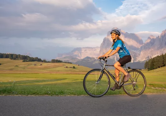 Guest cycling on road, meadow and large mountain in background.