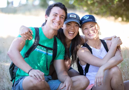 Three guests smiling for camera among yellow, grassy meadow.
