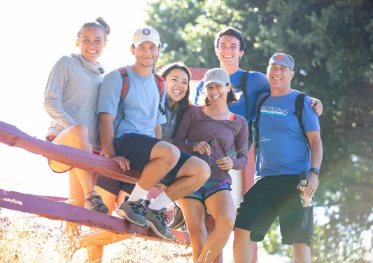 Six guests during sunset, three sitting on fence.
