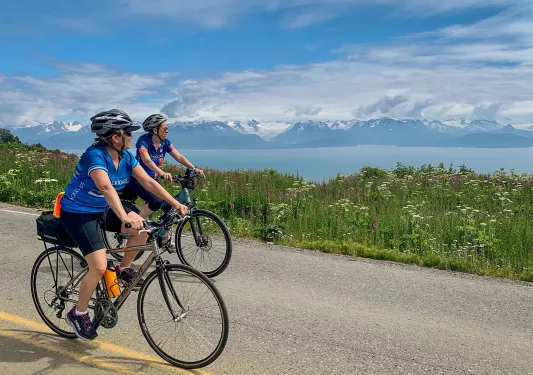 Two guests on road, cycling next to large lake. 